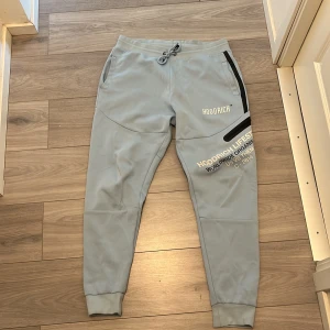 Ljusblå mjukisbyxor från Hoodrich - Snygga ljusblå mjukisbyxor från Hoodrich med tryck på benet och logga framtill. Byxorna har snörning i midjan, svarta detaljer vid fickorna och muddar vid bensluten. Perfekta för en chill och sportig stil.