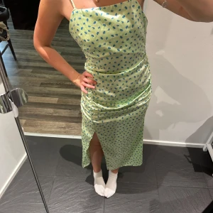 Ljusgrön blommig midiklänning Zara - Superfin ljusgrön midiklänning från Zara med blått blommönster. Klänningen har smala axelband som korsas i ryggen, slits framtill och figurnära passform. Materialet är glansigt och känns som satin, perfekt för sommarens alla tillfällen. Ens bandet sitter lite mer löst, men det är enkelt lagat och syns knappt 🥰se bild