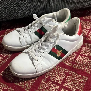 G skor  -  Ace sneakers i vitt skinn med klassiska gröna och röda ränder på sidan och broderad guldfärgad bi. Baksidan 