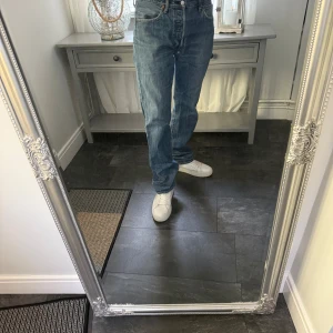 Levi's 501 blå jeans straight fit, vintage - Klassiska Levi's 501 jeans i ljusblå denim med rak passform och hög midja. Jeansen har fem fickor, knappgylf och ikonisk läderpatch bak i midjan. Perfekta för en avslappnad och tidlös stil.
