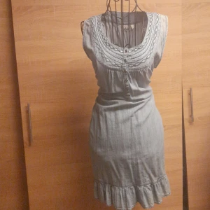 Ljusblå kort klänning från Isolde - Supersöt ljusblå kort klänning från Isolde med broderade detaljer och knappar framtill. Ärmlös modell med volangkant nertill och rundad halsringning. Perfekt för dig som gillar en feminin och avslappnad stil.