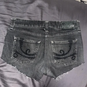 Svarta jeansshorts med mönster bakficka  - Snygga svarta jeansshorts från MAC snygga kanter och coola broderade detaljer på bakfickorna. Klassisk femficksmodell med låg midja och slitna detaljer för en edgy vibe. Perfekta till sommaren och lätta att matcha med allt. 
