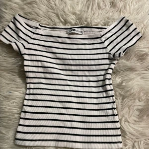 Randig offshoulder topp från SisterS - Superfin ribbad offshoulder topp från SisterS i vitt med svarta horisontella ränder. Toppens smala passform och korta ärmar ger en snygg och trendig look. Perfekt att matcha med jeans eller kjol för en cool stil.