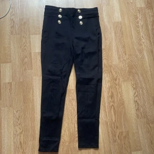 Svarta högmidjad byxa från Zara - Superfin byxa från Zara med hög midja och  guldknappar framtill. Byxorna har en slim passform och är tillverkade i ett stretchigt material som sitter skönt. Knappt använd.
