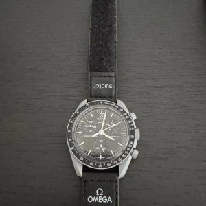 Omega x Swatch Speedmaster MoonSwatch - Säljer en svart Omega x Swatch Speedmaster MoonSwatch med klassisk rund boett och svart textilband. Klockan har tydliga vita detaljer på urtavlan och tachymeter-skala runt ringen. Levereras med originalbox och garantikort från 2023.