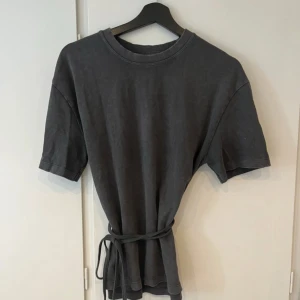 Zara topp med knytning  - Cool svart t-shirt med rund hals och korta ärmar. T-shirten har ett snyggt knytband i midjan som ger en unik och trendig look. 