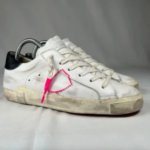 Philippe Model PSRX - Snygga vita sneakers från Philippe Model med svart häl och cool rosa broderad detalj på sidan. Skorna har snörning, platt sula och är tillverkade i skinn. Perfekta för dig som gillar streetstyle med en twist.