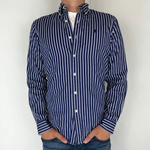 Ralph Lauren Skjorta - Nu har vi nöjet att erbjuda en klassisk  skjorta från det välkända varumärket Ralph Lauren. Plagget är i storlek Small och är i mycket gott skick, utan några synliga defekter. Modellen på bilden är 182 cm lång och väger 75 kg, vilket kan ge en god indikation på tröjans passform.