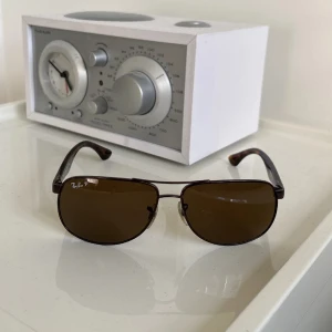 Ray-Ban solglasögon pilot - Säljer då ett par snygga Ray-Ban solglasögon i klassisk aviator-modell med bruna polariserade glas och bruna skalm med s. Metallbåge framtill och tydlig Ray-Ban-logga på linsen och skalmen. Perfekta för soliga dagar. Riktigt bra skick på dom inga konstigheter med bågen eller glaset. Kom med prisförslag, ingen box medföljes tyvärr.