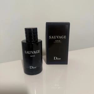 Dior Sauvage Parfum 100ml - Dior Sauvage Parfum i en snygg, mörkblå glasflaska med matchande kartong. Flaskan har en stilren, rund form och tydlig logga framtill. Parfymen är på 100 ml och har en lyxig känsla med magnetisk kork och minimalistisk design.