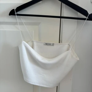 Vit bandeau topp från NLY One - Säljer en stilren vit bandeau topp från NLY One med tunna axelband och mjuk, slät yta. Perfekt för varma dagar eller lager på lager. Enkel och clean design som är lätt att matcha med allt.
