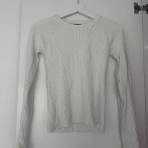 Vit ribbad tröja från Bik Bok - Supersöt vit ribbad tröja från Bik Bok i storlek M. Långa ärmar och fina volangdetaljer vid ärmsluten. Mjuk och stretchig rib.