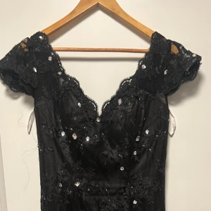 Svart långklänning med spets och paljetter - Säljer en svart långklänning med v-ringad hals och korta spetsärmar. 💕Klänningen är i spets med paljettstenar över hela tyget. Passformen är slim och materialet känns lyxigt, perfekt för bal eller fest. Pris går att diskutera💗