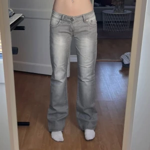 Gråa, Lågmidjade, bootcut Dzire jeans  - Ett par snygga grå jeans från Dzire med bootcut passform och låg midja. Jeansen har snygga detaljer på båda bakfickor. Knappen i fram samt den svarta etiketten där bak sitter lite löst men går enkelt att fixa. 