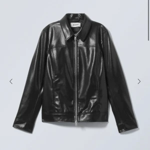 Svart skinnjacka från Weekday - Snygg svart skinnjacka från Weekday med klassisk krage och raka linjer. Jackan har dragkedja framtill och två sidfickor. Perfekt för dig som vill ha en stilren och tidlös look.