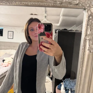 Grå kofta med knapp framtill - Säljer en stilren grå kofta med lång ärm och en knapp framtill vid halsen. Koftan är stickad och har en enkel, klassisk design som passar till det mesta. Perfekt att slänga över en topp för en chill look.