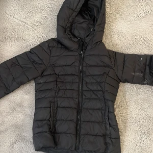 Svart pufferjacka från ONLY, S - Svart pufferjacka från ONLY i storlek S. Jackan har huva, dragkedja framtill och två fickor. Tillverkad i polyester och nylon, perfekt för kyliga dagar. Snygg quiltad design som ger en modern look.