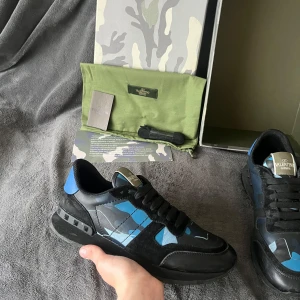 Valentino Rockrunners - Snygga Valentino Garavani Rockrunner sneakers i svart och blått med coolt camouflage-mönster. Skorna har svarta snören, platt sula och detaljer i mocka och skinn. Perfekta för dig som vill sticka ut med exklusiva och trendiga sneakers.