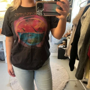 Svart t-shirt med smashing pumkins  - Cool svart t-shirt från Smashing Pumpkins med stort färgglatt tryck på framsidan. Trycket har motiv i rött, gult, blått och orange med texten 'Oceania'. Klassisk rund hals och korta ärmar. Perfekt för dig som gillar band-merch och vill sticka ut.