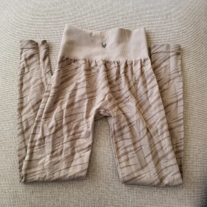Beige mönstrade seamless träningstights - Snygga beige leggings med zebramönster och bred, hög midja. De är sömlösa och har en mjuk, stretchig känsla som passar perfekt till träning eller chill. Diskret logga framtill på linningen. Lite noppriga i rumpan därav priset. Storlek XS/ S