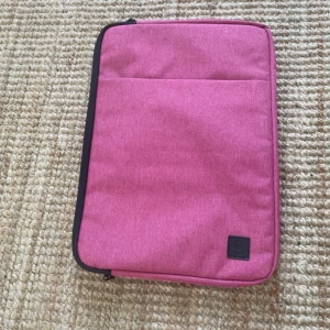 Rosa datorväska från Rabta - Säljer en stilren rosa datorväska från Rabta. Väskan har en enkel, rektangulär form med svart dragkedja och en praktisk ytterficka framtill. Tillverkad i tålig polyester och passar perfekt för att bära din laptop till skolan eller jobbet.