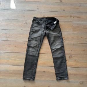 Svarta Jack & Jones tapered jeans - cool look☑️ - Svarta Jack & Jones tapered jeans i strl 28/30. Sitter bra och har ett slitet benslut - ger en ren och snygg look. Har ett litet hål, en liten fläck och en spricka på patchen (skriv för bild) men påverkar inte helhetsbilden. 🍂Perfekta för hösten ☑️Snygg passform ✅Endast 249kr!🎁Fri frakt resten av veckan!