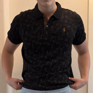 Svart mönstrad piké från Ralph Lauren - Mönstrad mörk ralph lauren piké. Tröjan är helt ny. säljer även ut andra saker från min gaderob så kolla gärna min sida och se om du hittar något du gillar!