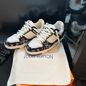 Louis Vuitton svartvita sneakers strl 42 - Säljer ett par Louis Vuitton sneakers i svart och vitt med ikoniskt monogrammönster. Skorna har snörning, rund tå och platt sula. Tillverkade i skinn och textil med tydliga LV-detaljer på sidorna och sulan. Riktigt snygga och sticker ut i mängden.