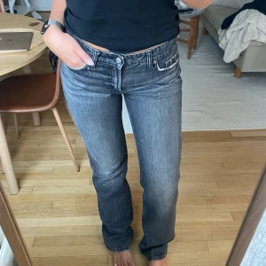 Grå jeans med låg midja - Säljer ett par  jeans från Zara i grå tvätt med låg midja och raka ben. Klassisk femficksmodell med vita kontrastsömmar och detaljer vid fickorna. Jeansen har en avslappnad passform och är tillverkade i slitstarkt denim.