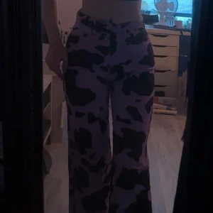 Lila ko-mönstrade jeans - Säljer ett par lila jeans med svart, ko-mönster. Byxorna har hög midja och raka, vida ben. Materialet känns mjukt vilket gör dem bekväma att bära hela dagen.
