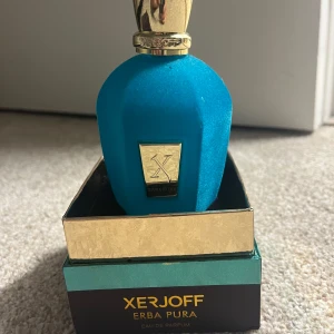 Xerjoff Erba Pura Eau de Parfum - Lyxig parfym från Xerjoff, Erba Pura, i en unik blå sammetsflaska med gulddetaljer och elegant guldlock. Flaskan har en exklusiv känsla och levereras i en snygg ask med guldfärgade och turkosa inslag. Perfekt för dig som gillar exklusiva dofter.