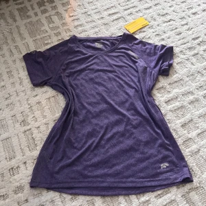 Lila tränings-tshirt  - Sportig lila t-shirt från Mountain Works med rund hals och korta ärmar. Tillverkad i ett lätt och snabbtorkande syntetmaterial, perfekt för träning. Diskret logga på bröstet och nedtill. Snygg passform som sitter skönt på kroppen.