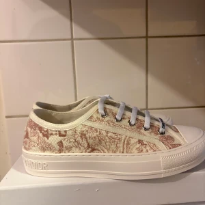 sneakers Beige rosa - Snygga sneakers från  i beige och ljusrosa med broderat mönster och tydlig logga på tungan och sulan. Skorna har vita snören, rund tå och platt sula. Tillverkade i textil med exklusiv känsla och detaljer i vitt gummi.