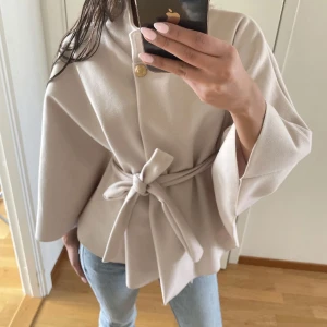 MISSAY poncho - Säljer en superfin beige kappa med knytbälte i midjan och vida ärmar. Jackan har en snygg guldig knapp upptill och är i ett mjukt, stilrent material. 