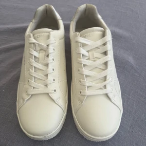 Vita sneakers från ONLY med glitterdetalj - Snygga vita sneakers från ONLY med silvriga detaljer och glittrig häl. Skorna har klassisk snörning, rund tå och platt sula. 