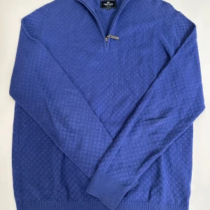 Blå stickad half zip-tröja Park Lane - Snygg blå stickad tröja från Park Lane med diskret rutmönster och half zip-dragkedja vid kragen. Tröjan har lång ärm, ribbade muddar och en klassisk passform. Perfekt för dig som gillar stilren och bekväm look. Storlek M passar även large.