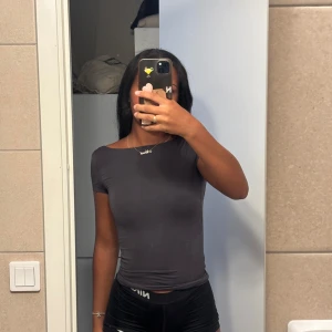 Mörkgrå topp med öppen rygg - Säljer en mörkgrå, tight topp med korta ärmar och riktigt snyggt öppen rygg. Toppen har en rundad hals och sitter slim på kroppen. Perfekt om du vill ha en enkel men ändå cool look. Materialet känns mjukt och stretchigt, troligen bomull eller polyester.