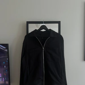 Svart overshirt  - Stilren svart overshirt med silverfärgad dragkedja framtill och två stora bröstfickor. Märke: HM. Storlek M