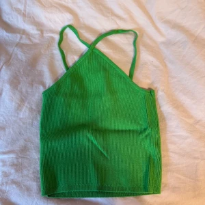 Grön ribbad linnetopp - Snygg grön ribbad linnetopp med smala axelband som korsas i framtill. Toppen är croppad och har en tight passform, perfekt för varma dagar eller lager på lager. Materialet är stretchigt och mjukt, vilket gör den superbekväm att bära.