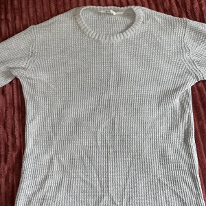 Grå stickad tröja från H&M - Säljer en stilren grå stickad tröja från H&M med rund halsringning och ribbade muddar. Tröjan är tillverkad i en blandning av bomull och polyester och har en klassisk, enkel design som passar perfekt till lager-på-lager-stil.