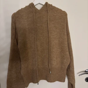 Beige stickad hoodie med snörning - Mysig beige stickad hoodie med långa ärmar och ribbade muddar. Tröjan har huva och snörning framtill, samt en avslappnad passform. Perfekt för lager-på-lager och chill dagar. Storlek s men passar både större och mindre