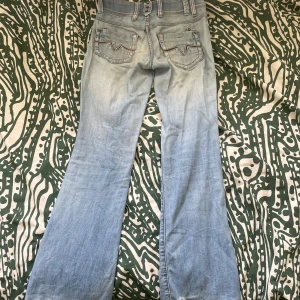 Ljusblå bootcut jeans med broderade fickor - Säljer ett par ljusblå vintage bootcut jeans med snygga broderade bakfickor. Jeansen är lågmidjade. Slitna där bak (se bild 3) i form av tunna slitna trådar).❤️
