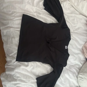 Svart blus med knyt och vida ärmar - Stilren svart blus med v-ringning och knyt framtill. Blusen har långa, vida ärmar. Den passar även en L