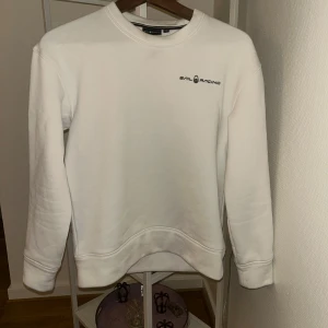 Vit sweatshirt från Sail Racing - Vit sweatshirt från Sail Racing med diskret logga på bröstet och en liten logga i nacken. Klassisk rund halsringning och långa ärmar. Mjuk insida och ribbade muddar vid ärmslut och nederkant. Perfekt för en clean och sportig look.