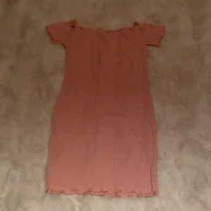 Rosa ribbad t-shirt med volang - Supersöt rosa  T-shirt med ribbad struktur och volangdetaljer vid halsringning och fåll. T-shirten har korta ärmar och en figurnära passform som ger en trendig look. Perfekt för dig som gillar en feminin och enkel stil.