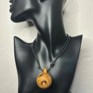 Retro halsband med snidat trä – 70-talets bohemiska charm -  Unikt retrohalsband med skulpturalt hänge i handskuret trä – tre urholkade kulor inuti varandra, tillverkade ur ett enda trästycke. Hänger i justerbar svart textilsnodd. Troligen från sent 70-tal eller tidigt 80-tal – perfekt för dig som gillar bohemisk stil, hantverk och naturliga material.  Priset är redan lågt – ett riktigt fynd – så jag prutar inte. Men jag erbjuder bra rabatt vid köp av flera saker.  ⸻  