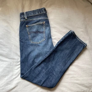 Nudie Jeans Gritty Jackson Blue Soil 32/32 - Snygga blå jeans från Nudie Jeans, modell Gritty Jackson i färgen Blue Soil. Klassisk femficksdesign med kontrastsömmar och vågig brodyr på bakfickan. Tillverkade i 100% bomull för en autentisk jeanskänsla. Perfekta för dig som gillar stilrena och tidlösa jeans. Bara att höra av sig om man har några frågor om mått osv🤗