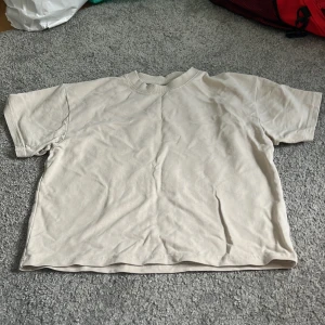 Beige t-shirt från Lindex - En basic beige t-shirt från Lindex i mjuk bomull. Klassisk rund halsringning och korta ärmar, perfekt för en clean och enkel stil. Passar dig som gillar neutrala färger och vill ha en skön t-shirt till vardags.