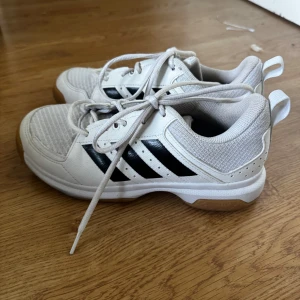 Vita Adidas sneakers med svarta ränder - Snygga vita Adidas sneakers med klassiska svarta ränder på sidorna och ljusbrun gummisula. Ovandelen är i mesh och syntet för bra andningsförmåga. Skorna har snörning och rund tå, perfekt för dig som gillar sportig stil. Kan mötas upp i Norrköping ☺️