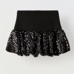 Svart paljettkjol med volang från Zara - Supersnygg svart kortkjol med glittrande paljetter och volang nedtill. Kjolen har en bred, stretchig midja som sitter bekvämt och ger en cool siluett. Perfekt för dig som vill sticka ut och glänsa lite extra.